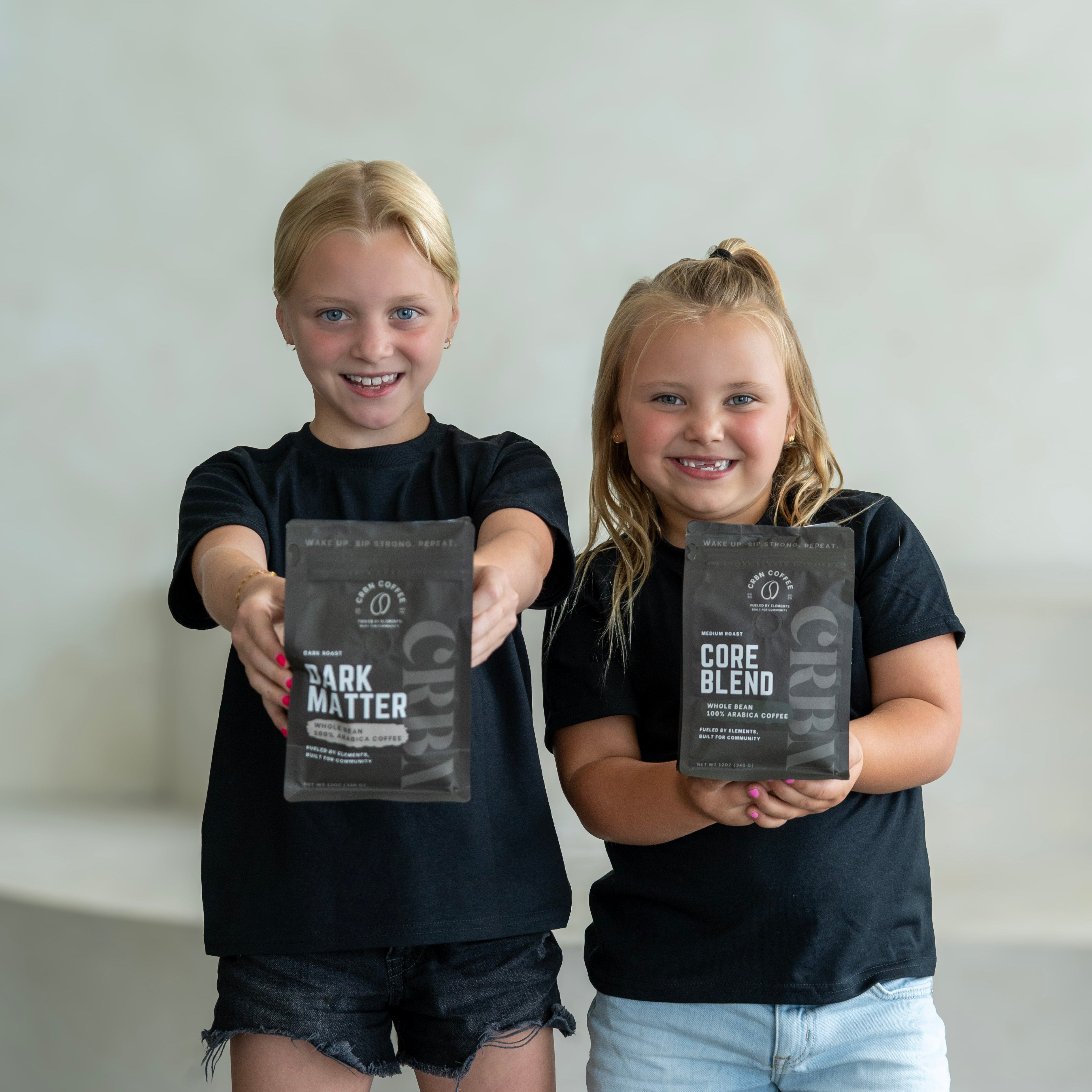 Two children holding dark matter protein powder packets against a plain background